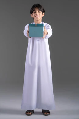 Gift giving during holidays and occasions, expressing warmth and love, a portrait of a smiling Emirati Gulf Arab boy wearing traditional attire holding a blue gift box, gray background. Gift giving during holidays and occasions, expressing warmth and love, a portrait of a smiling Emirati Gulf Arab boy wearing traditional attire holding a blue gift box, gray background.