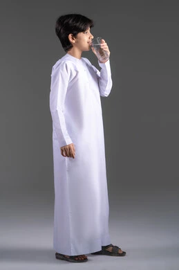 التخلص من سموم الجسم، الحفاظ على صحة الكلى ومعالجتها، بورتريه لولد عربي خليجي اماراتي يرتدي الكندورة  يشرب كأس من المياه، أهمية شرب الماء النقي للحصول على بشرة نضرة، المحافظة على سلامة الجهاز المناعي، الجسم بالطول الكامل، خلفية رمادية