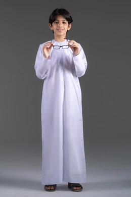 وضع نظارة لتحسين الرؤية ، الاهتمام بالمظهر الخارجي, بورتريه لولد عربي خليجي اماراتي يرتدي الكندورة  يقوم بارتداء النظارات الطبية ينظر إلى الكاميرا بإيماءات السرور والسعادة، مفهوم اضعف النظر ، الجسم بالطول الكامل, خلفية رمادية