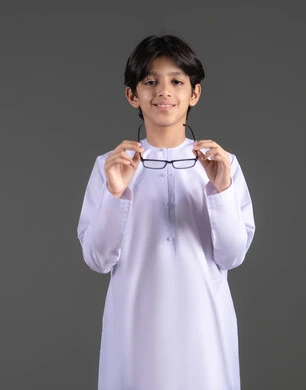 مفهوم ضعف النظر،وضع نظارة لتحسين الرؤية ، الاهتمام بالمظهر الخارجي, بورتريه لولد عربي خليجي اماراتي يرتدي الكندورة  يقوم بارتداء النظارات الطبية ينظر إلى الكاميرا بإيماءات السرور والسعادة،  خلفية رمادية