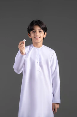 بورتريه لولد  عربي خليجي اماراتي يرتدي الزي التقليدي، ينظر الى الكاميرا بايماءات السرور ويحمل بيده سماعة بلوتوث جوال حديثه، مفهوم إستخدام إكسسوارات الجهاز المحمول، خلفيه رماديه