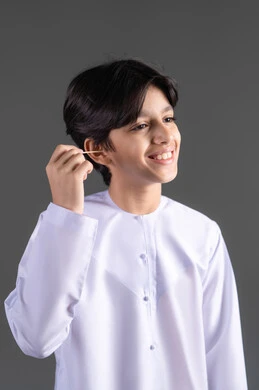 روتين نظافة الأذنين اليومية، العناية والاهتمام بصحة الأذن، استخدام أعواد ونكاشات القطن، بورتريه لفتى عربي خليجي اماراتي يرتدي الكندورة يقوم وضع نكاشة قطنية داخل أذنه، الاهتمام المظهر الخارجي، خلفية رمادية