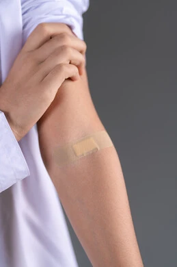 دور الضمادات الطبية في تخفيف الألم, إيماءات تدل على وجود الأوجاع, بورتريه مقرب لفتى عربي خليجي اماراتي يرتدي الكندورة يشير إلى لصاقة صغيرة موجودة على يده, خلفية رمادية