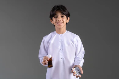 الالتزام باتخاذ الأدوية في الوقت المناسب لها, مفهوم الاستفادة من الدواء الموصوف, بورتريه لفتى عربي خليجي اماراتي يرتدي الكندورة يحمل زجاج دواء عاتمة وشريط  حبوب، الإصابة بالمرض والتوعك, خلفية بيضاء