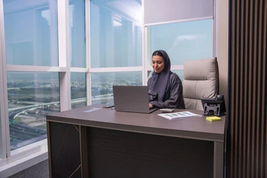 ايماءات التركيز والاندماج، استخدام جهاز تقني حديث ومتطور، مهنة ووظيفة نسائية، ادارة الأعمال وانجاز المهام المطلوبة، إمرأة عربية خليجية اماراتية محجبة ترتدي عباءة تجلس على المكتب تستخدم الحاسوب المحمول