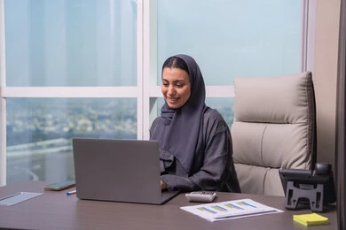 The use of a modern and advanced technical device, a profession and job for women, business management and completing required tasks, an Arab Gulf Emirati woman wearing a hijab and an abaya sitting at a desk using a laptop, gestures of focus and engagement. The use of a modern and advanced technical device, a profession and job for women, business management and completing required tasks, an Arab Gulf Emirati woman wearing a hijab and an abaya sitting at a desk using a laptop, gestures of focus and engagement.