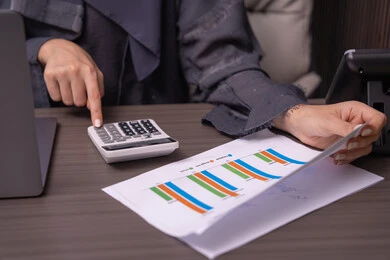 مهن ووظائف مكتبية، قسم التحليلات والإحصائيات البيانية، صورة مقربة ليد امراه عربية خليجية اماراتية ترتدي العباءة تعمل على إدارة الحسابات، إستخدام جهاز الحاسوب المحمول، إستخدام الآلة الحاسبة لإجراء العمليات الحسابية، البورصة والإستثمار المالي