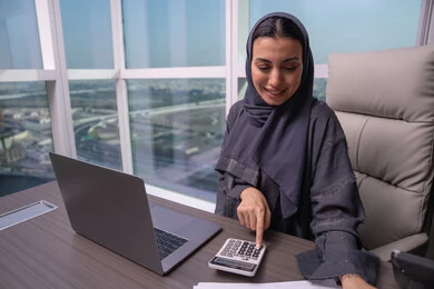 إستخدام جهاز الحاسوب المحمول، قسم التحليلات والإحصائيات البيانية،امراه عربية خليجية اماراتية ترتدي العباءة و الحجاب تعمل على إدارة الحسابات، مهن ووظائف مكتبية، إستخدام الآلة الحاسبة لإجراء العمليات الحسابية، البورصة والإستثمار المالي