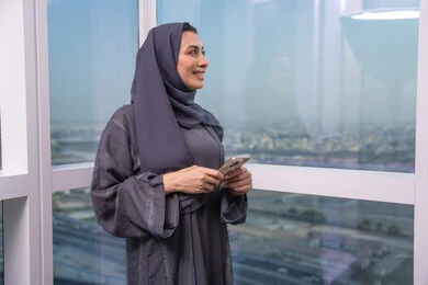 النظر الى شيء ما، الدردشة والتواصل مع التواصل مع الأصدقاء اونلاين، تصفح وسائل التواصل الاجتماعي باستخدام الجوال، امراة عربية خليجية اماراتية محجبة ترتدي العباءة و الحجاب تقف بجانب النافذة تمسك بيديها الهاتف المحمول، تعابير وايماءات الفرح والسرور النظر الى شيء ما، الدردشة والتواصل مع التواصل مع الأصدقاء اونلاين، تصفح وسائل التواصل الاجتماعي باستخدام الجوال، امراة عربية خليجية اماراتية محجبة ترتدي العباءة و الحجاب تقف بجانب النافذة تمسك بيديها الهاتف المحمول، تعابير وايماءات الفرح والسرور