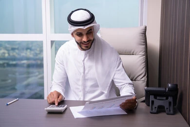 تفسير المعلومات الإحصائية المستخرجة، رجل عربي خليجي اماراتي يرتدي الكندورة و الغتره يعمل على الحاسب لانجاز المهام في المكتب، استخدام الالة الحاسبة لاجراء العمليات الحسابية، وظيفة مكتبية في شركات الخليج العربي