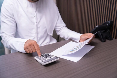 Processing statistical data results, a close-up image of the hand of an Arab Gulf Emirati man wearing a kandura working on a computer to complete tasks in the office, using a calculator to perform calculations, an office job in Gulf Arab companies.