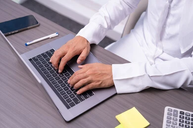 Communicating with clients remotely, integrating modern and advanced technologies with work, professions and administrative office jobs, a close-up image of the hand of an Emirati Gulf Arab man wearing a kandura sitting in the office and typing on the keyboard, sending an email via the computer.