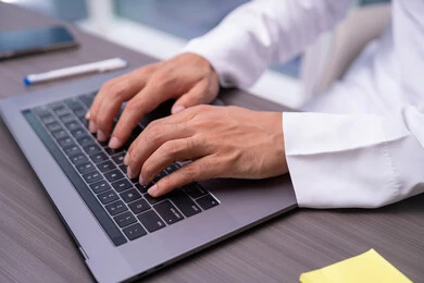 Integrating modern and advanced technologies with work, professions and administrative office jobs, communicating with clients remotely, a close-up image of the hand of an Arab Gulf Emirati man wearing a kandura sitting in the office and typing on the keyboard, sending an email via the computer.