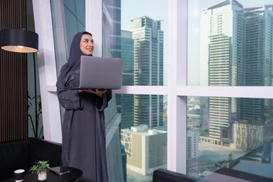 بيئة مهنية مريحة في مؤسسات الإمارات، ايماءات السعادة و السرور، تنظيم اجتماع عبر الإنترنت ,امراه عربيه خليجيه اماراتية ترتدي العباءة و الحجاب تقوم بتصفح مواقع أخبار السوشال ميديا عبر جهاز الحاسوب, استخدام الأجهزة والتقنيات الحديثة والمتطورة