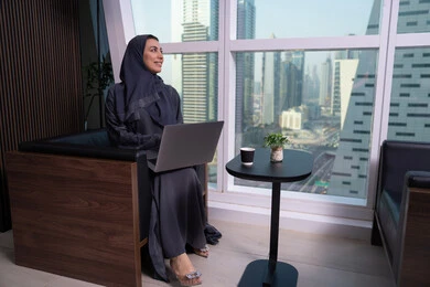 Looking at something, a comfortable work environment in Emirati companies, holding a business meeting online, an Arab Gulf Emirati woman wearing an abaya and hijab browsing social media news sites on a computer, using modern and advanced devices and technologies.