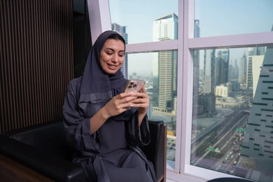 Exchanging conversations with family and friends, expressions and gestures of integration and joy, using advanced modern technology in professional life, an Arab Gulf Emirati woman wearing a hijab and abaya working on a mobile phone, a profession and office job.