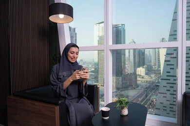 إجراء محادثات مع العائلة والأصدقاء، تعابير وايماءات الاندماج والسرور، استخدام التقنية الحديثه المتطورة في الحياة العملية، امراة عربية خليجية اماراتية ترتدي الحجاب والعباءة تقوم بالعمل على الهاتف المحمول، مهنة ووظيفة مكتبية