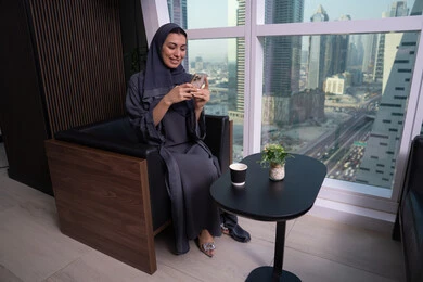 Expressions and gestures of integration and joy, using advanced modern technology in professional life, an Arab Gulf Emirati woman wearing a hijab and abaya working on a mobile phone, a clerical job and profession, chatting with family and friends.