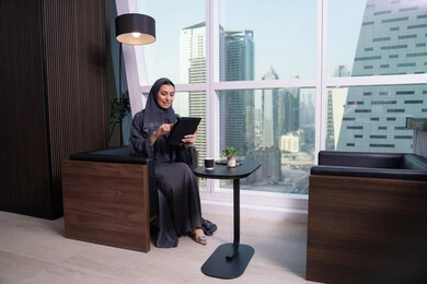 انجاز وادارة المهام باستخدام جهاز تقني حديث ومتطور، مهنة ووظيفة مكتبية، القيام بمحادثة مرئية، العمل عن بعد, تعابير السعادة و السرور، امراة عربية خليجية اماراتية ترتدي الحجاب والعباءة تعمل على جهاز التابلت