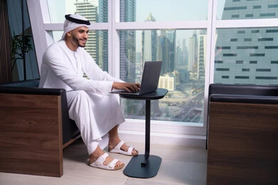 الضغط على مفاتيح الكيبورد، دمج العمل مع التقنية والتكنولوجيا، إدارة شؤون الأعمال وتنظيمها عبر الأجهزة التقنية، رجل  عربي خليجي اماراتي يرتدي الكندورة و الغتره يجلس على كرسي يعمل على الحاسوب المحمول، مهن ووظائف إدارية مكتبية