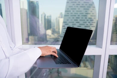 Typing on the keyboard, managing and organizing business affairs through technical devices, a close-up image of the hand of an Arab Gulf Emirati man wearing a kandura working on a laptop inside the company headquarters, administrative and office jobs, integrating work with technology and technology.