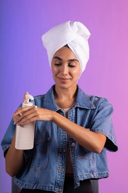 العناية بالجلد من خلال الكريمات التجميلية، الاهتمام بالمظهر الخارجي، بورتريه مقرب لامرأة عربية خليجية سعودية ترتدي الزي الكاجوال و منشفة بيضاء تحمل بيدها علبة كريم الترطيب، خلفية ملونه