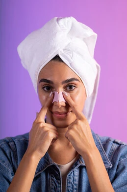 إزالة الرؤوس السوداء والطبقات الميتة، استخدام ماسك تنظيف المسام ومكون تجميلي، مفهوم العناية بنضارة وتحسين البشرة، بورترية مقرب لإمرأة عربية خليجية سعودية ترتدي الزي الكاجوال تضع منشفة الرأس تستخدم لصاقة الأنف، خلفية ملونه