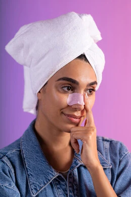 مفهوم العناية بنضارة وتحسين البشرة، استخدام ماسك تنظيف المسام ومكون تجميلي، التخلص من الرؤوس السوداء والجلد الميت، بورترية مقرب لإمرأة عربية خليجية سعودية ترتدي الزي الكاجوال تضع منشفة الرأس تستخدم لصاقة الأنف، خلفية ملونه