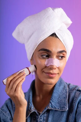 مفهوم العناية والإهتمام بنضارة وتحسين البشرة، ماسك تنظيف المسام، إستخدام أداة شفط لحب الشباب، بورترية مقرب لإمرأة عربية خليجية سعودية ترتدي الزي الكاجوال تضع منشفة الرأس تستخدم لصقات الأنف للتخلص من الرؤوس السوداء والجلد الميت، خلفية ملونه