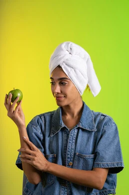 العناية باللياقة الجسدية والتوازن البدنى، اتباع نظام غذائي صحي وتناول الفاكهة الطازجة، بورتريه لشابة عربية خليجية سعودية ترتدي الزي الكاجوال و منشفة الرأس تحمل بيدها تفاحه خضراء، خلفية ملونه