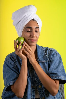 السعي للحفاظ على الرشاقة واللياقة، اتباع نظام غذائي صحي وتناول الفاكهة الطازجة، بورتريه لشابة عربية خليجية سعودية ترتدي الزي الكاجوال و منشفة الرأس تحمل بيدها تفاحه خضراء، خلفية ملونه