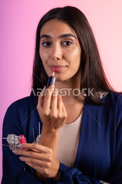 صالون تجميلي للنساء، التسويق لمنتجات التجميل، بورترية مقرب لمرأة عربية خليجية سعودية ترتدي الزي الكاجوال  تحمل إحدى أدوات التجميل (قلم أحمر الشفاة)، مرأة خبيرة بمستحضرات التجميل، متجر بيع مستحضرات التجميل عبر الإنترنت، مفهوم الإهتمام بالجمال والبشرة، ادوات مكياج تتوريال، خلفية ملونه