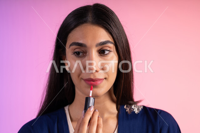 صالون نسائي للعناية بالجمال، التسويق لمنتجات التجميل، بورترية مقرب لمرأة عربية خليجية سعودية ترتدي الزي الكاجوال  تحمل إحدى أدوات التجميل (قلم أحمر الشفاة)، مرأة خبيرة بمستحضرات التجميل، متجر بيع مستحضرات التجميل عبر الإنترنت، مفهوم الإهتمام بالجمال والبشرة، ادوات مكياج تتوريال، خلفية ملونه