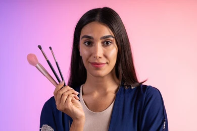 ادوات ميكاب تتوريال، مفهوم الإهتمام بالجمال والبشرة، التسويق لمنتجات التجميل، متجر بيع مستحضرات التجميل، بورتريه مقرب لمرأة عربية خليجية سعودية ترتدي الزي الكاجوال تحمل مجموعة من فرش المكياج، خلفية ملونه