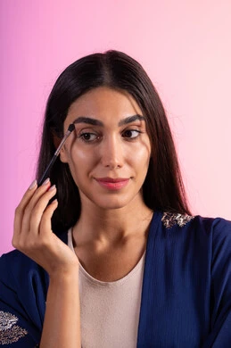 التسويق لمنتجات التجميل، إستخدام إحدى أدوات التجميل ( فرشاة ظل العيون ) ، بورتريه مقرب لامراة عربية خليجية سعودية ترتدي الزي الكاجوال تضع ميكاب ، الإهتمام بالجمال والمظهر الخارجي ، أدوات مكياج تتوريال ، خلفية ملونه