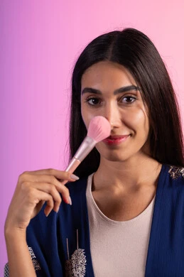 استخدام أدوات تجميل نسائيه عصريه، بورتريه مقرب لفتاه عربيه سعودية خليجيه ترتدي الزي الكاجوال تحمل بيدها فرشاة توريد الخدود ، صالون نسائي راقي،مفهوم الانوثه والاهتمام بالمظهر الخارجي، مكياج وميكاب تتوريال، التسويق لمنتجات التجميل، خلفية ملونه