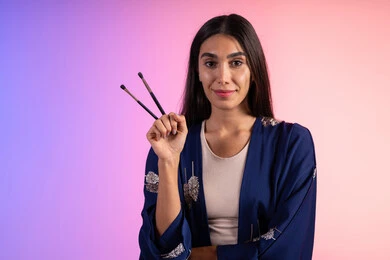 متجر بيع مستحضرات التجميل، بورتريه مقرب لمرأة عربية خليجية سعودية ترتدي الزي الكاجوال تحمل مجموعة من فرش المكياج، التسويق لمنتجات التجميل، مفهوم الإهتمام بالجمال والبشرة، ادوات ميكاب تتوريال، خلفية ملونه