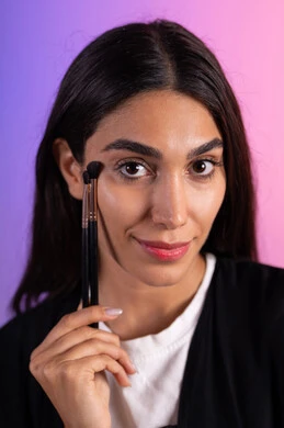 العناية بالمظهر الشخصي والجمال، أدوات مكياج تتوريال ، التسويق لمنتجات التجميل، إستخدام إحدى أدوات التجميل ( فرشاة ظل العيون ) ، بورتريه مقرب لامراة عربية خليجية سعودية ترتدي الزي الكاجوال تضع ميكاب، خلفية ملونه