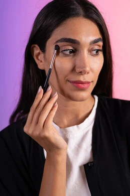 Marketing for beauty products, using one of the beauty tools (eyeshadow brush), a close-up portrait of a Saudi Gulf Arab woman wearing casual attire applying makeup, focusing on beauty and appearance, makeup tutorial tools, colorful background.