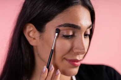 إستخدام إحدى أدوات التجميل ( فرشاة ظل العيون ) ، بورتريه مقرب لامراة عربية خليجية سعودية ترتدي الزي الكاجوال تضع ميكاب ، التسويق لمنتجات التجميل ، الإهتمام بالجمال والمظهر الخارجي ، أدوات مكياج تتوريال ، خلفية ملونه