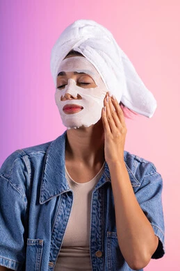 استخدام منتجات العناية الجمالية، روتين العناية وتحسين نضارة البشرة، خطوات تنظيف وتفتيح وترطيب الجلد, بورتريه مقرب لامراة عربية خليجية سعودية ترتدي الزي الكاجوال تضع منشفة الرأس تضع القناع التجميلي على الوجه، خلفية ملونه