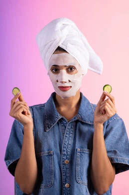 تطبيق مستحضرات التجميل ، مفهوم العناية والإهتمام بنضارة وتحسين البشرة ، بورتريه لمرأة عربية خليجية سعودية ترتدي الزي الكاجوال تضع منشفة الرأس تمسك بيديها قطع من الخيار، خلفية ملونه