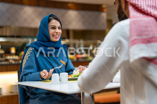 زوجان عربيان سعوديان خليجيان يجلسان في مطعم, الاستمتاع بتناول الطعام, حوارات ونقاشات على مائدة الطعام, مفهوم الاسره السعيده, قضاء اوقات ممتعه, عطلة نهاية الاسبوع, تعارف وبناء علاقات اجتماعيه, صداقات ومعارف