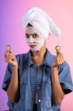 مفهوم العناية والإهتمام بنضارة وتحسين البشرة ، بورتريه لمرأة عربية خليجية سعودية ترتدي الزي الكاجوال تضع منشفة الرأس تمسك بيديها قطع من الخيار، إستخدام مكونات تجميلية، خلفية ملونه
