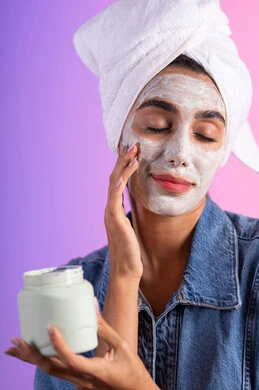 استعمال كريم تجميلي، مفهوم العناية بنضارة وتحسين البشرة، بورتريه مقرب لامرأة عربية خليجية سعودية ترتدي منشفة الرأس و الزي الكاجوال تمسك بيدها علبة جل الترطيب،خلفية ملونه