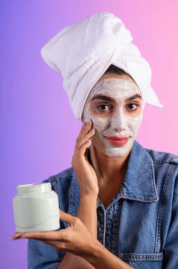 وضع كريم تجميلي، مفهوم العناية بنضارة وتحسين البشرة، بورتريه مقرب لامرأة عربية خليجية سعودية ترتدي منشفة الرأس و الزي الكاجوال تمسك بيدها علبة جل الترطيب،خلفية ملونه