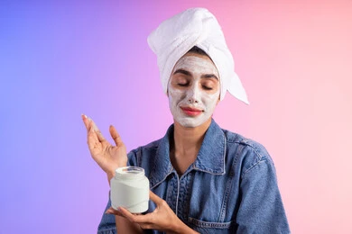 مفهوم العناية بنضارة وتحسين البشرة، استخدام كريم ومكون تجميلي، بورتريه مقرب لامرأة عربية خليجية سعودية ترتدي منشفة الرأس و الزي الكاجوال تمسك بيدها علبة جل الترطيب،خلفية ملونه