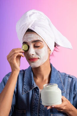 استخدام المكونات الطبيعية للعناية بالمظهر الخارجي، الاستعداد للاهتمام بنظافة ونضارة البشرة، تنظيف وتقشير الوجه، بورتريه مقرب لامرأة عربية خليجية سعودية ترتدي الزي الكاجوال ومنشفة بيضاء تحمل بيديها قطع من الخيار و كريم، خلفية ملونه