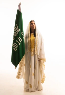 الاحتفال بيوم العلم السعودي11 مارس, ارتداء زي المنطقة الوسطى في المناسبات الوطنية، يوم بدينا 1727 م، ذكرى تأسيس الدولة السعودية الأولى 22 فبراير، بورتريه لإمرأة عربية خليجية سعودية ترتدي العباءة البيضاء المزخرفة تمسك راية وشعار المملكة بتعابير الفخر, الجسم بالطول الكامل، خلفية بيضاء