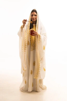 منتجات غذائية صحية ومفيدة صنعت في السعودية، بورتريه لامراة عربية خليجية سعودية ترتدي العباءة البيضاء المزخرفة تحمل بيدها ملعقة مغمورة من عسل النحل الطبيعي في وعاء زجاجي، يوم بدينا1727م، إرتداء أزياء المنطقة الجنوبية، ذكرى تاسيس الدولة السعودية22 فبراير، تعابير الفخر والسرور، الجسم بالطول الكامل، خلفية بيضاء